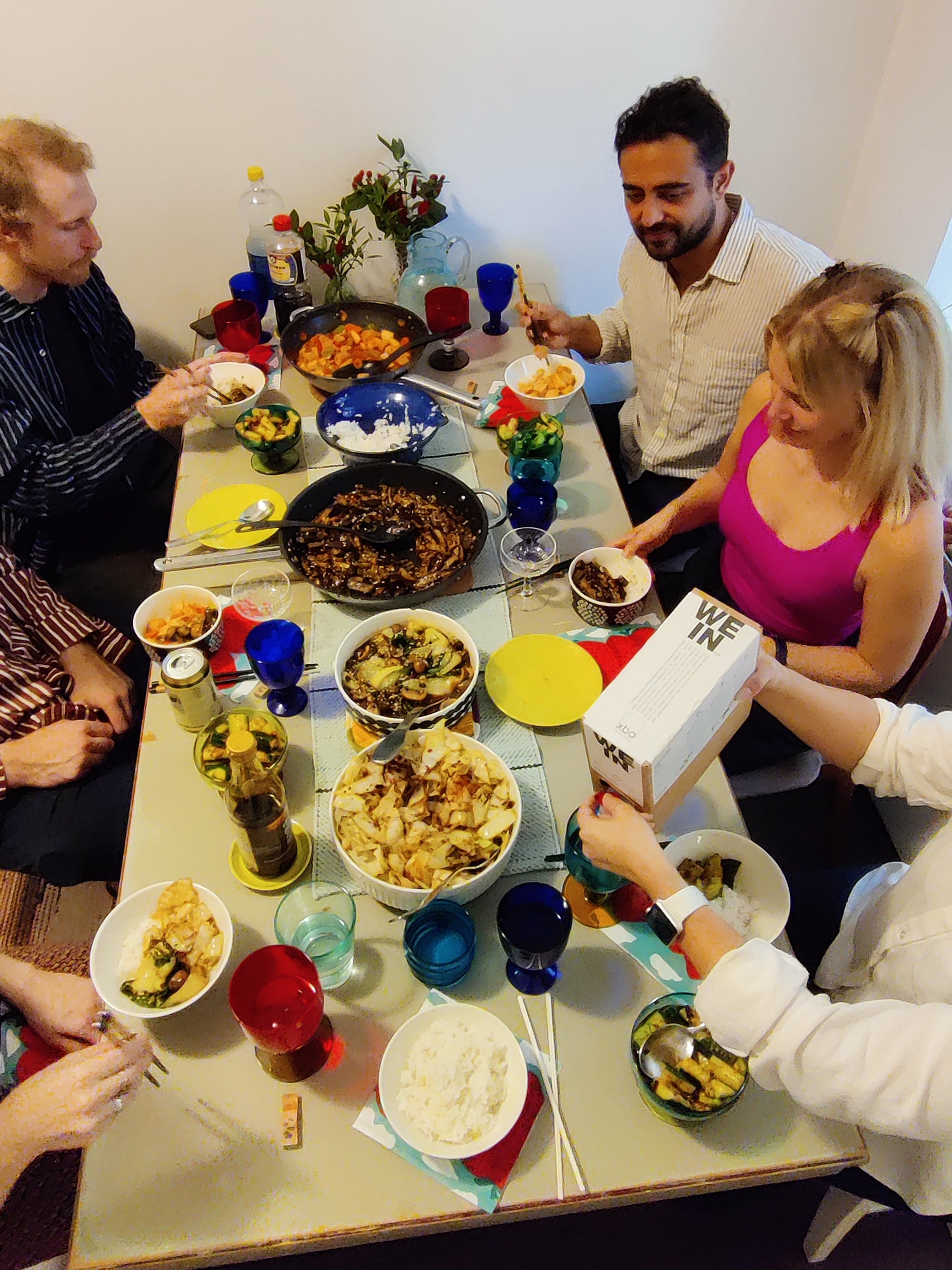 Gruppe von jungen Menschen sitzt zusammen an einem reichlich gedeckten Tisch. Sie genießen gute Speisen, Bag-in-Box Wein und freuen sich beim Zusammensein.